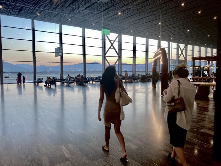 Milas-Bodrum Airport terminal interior at dusk with seating, windows, and departing passengers.